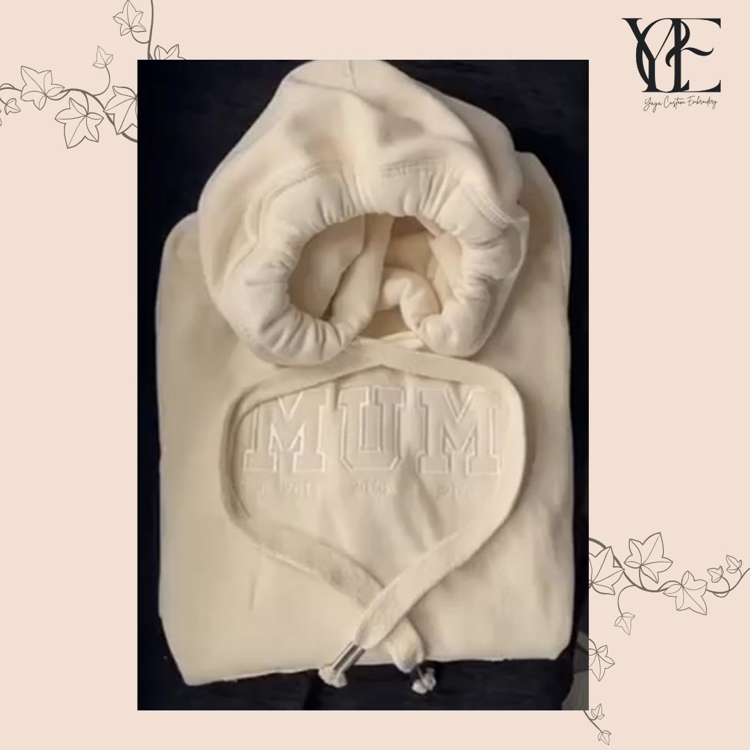 Close up of a vanilla colour hoodie with MUM embroidered at the front using college font