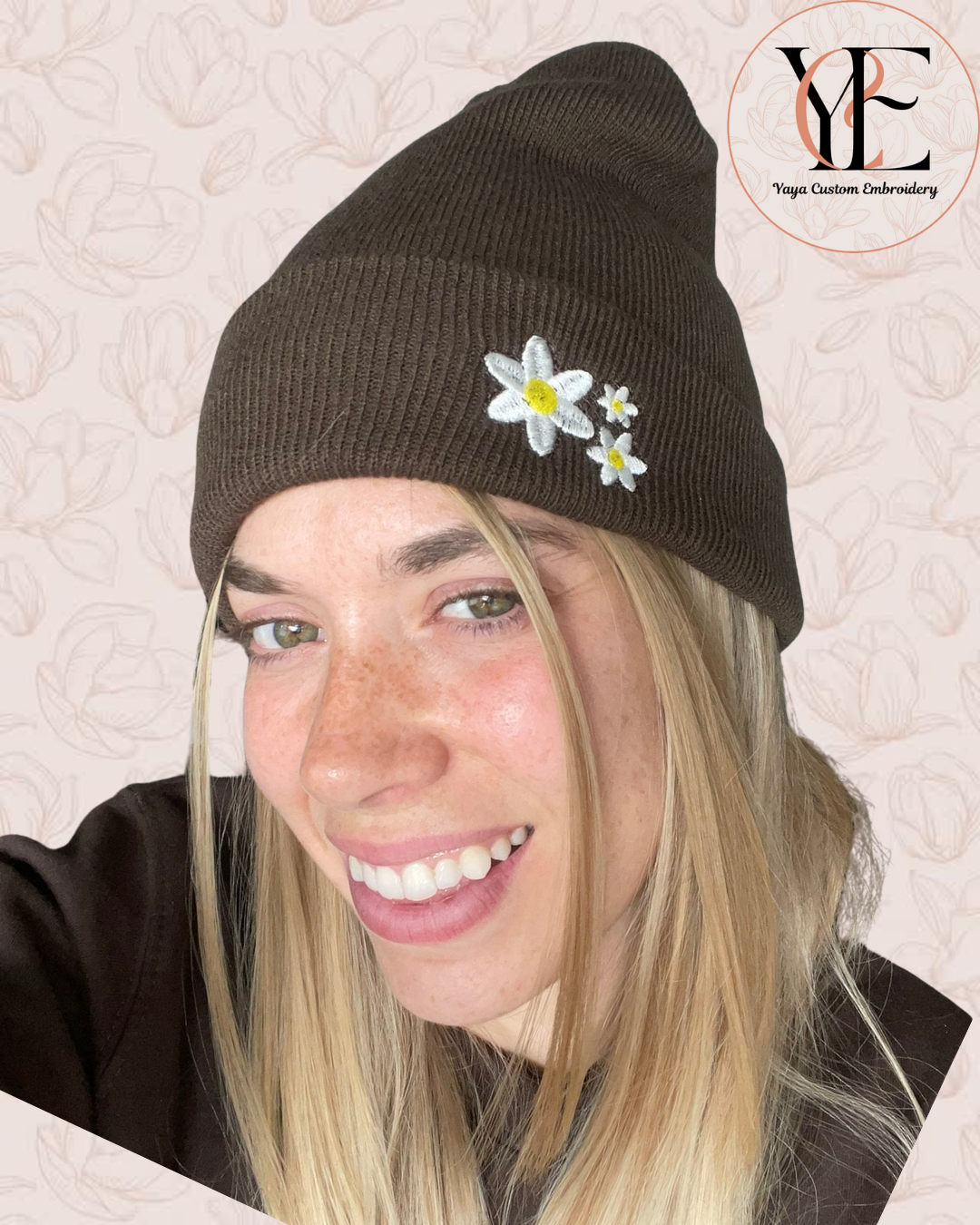 Person wearing a brown beanie with embroidered white daisies on a textured beige background