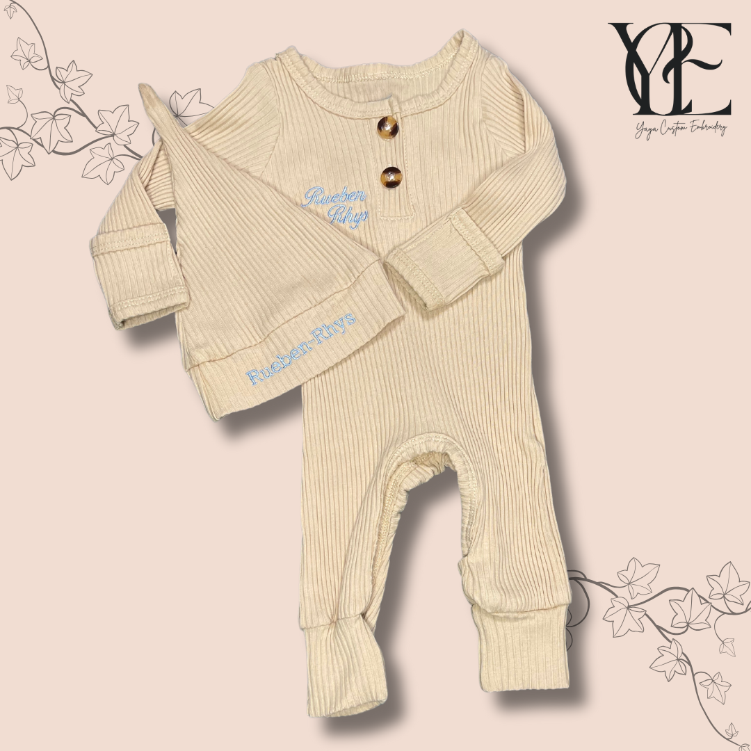 Custom embroidered babygrow and hat set in cream colour. Embroidered with the baby's name (Rueben) over the chest and on the hat. By Yaya Custom Embroidery.