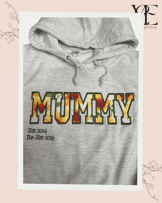Grey hoodie with MUMMY embroidered using Varsity font applique. The outline of the letters is in green matching the green of the sunflower applique material.
