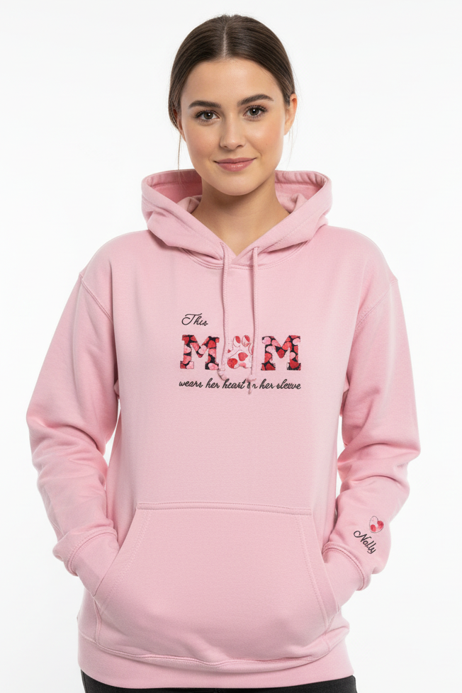 Woman wearing a pink hoodie with tHIS MUM wears her heart on her sleeve where the U is a paw design on a white background