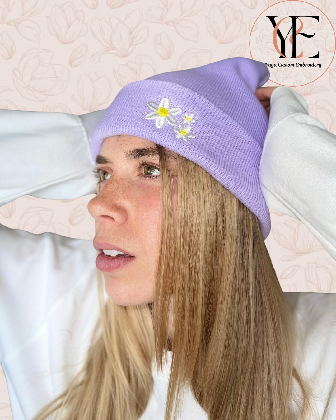 Person wearing a lavender beanie with embroidered flowers, branded 'YCE'.