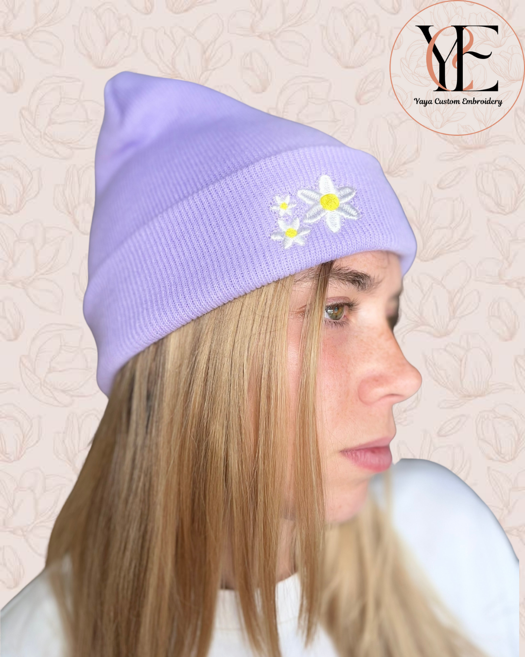 Person wearing a lavender beanie with embroidered flowers on a textured beige background