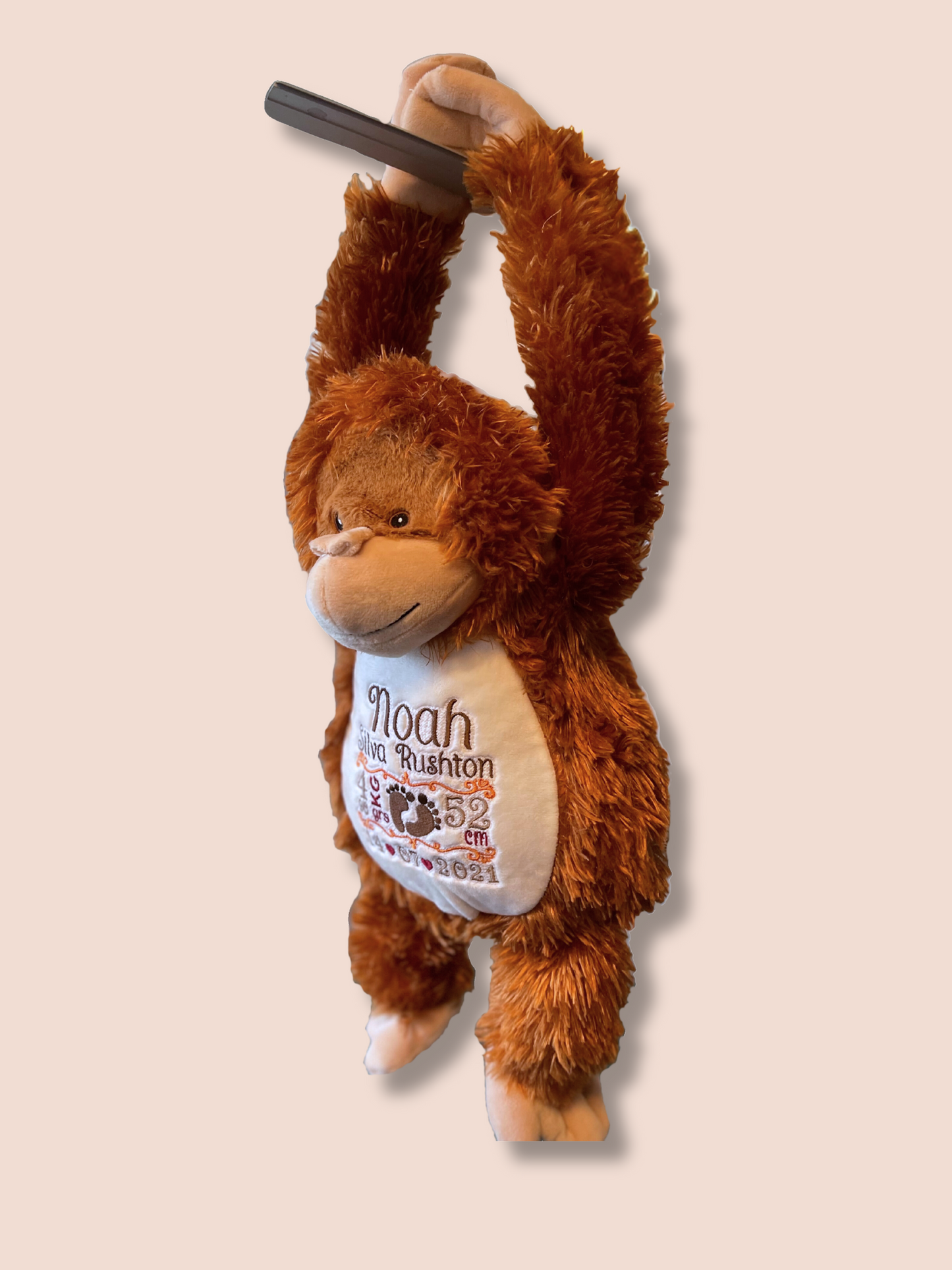 Soft toy orangutan hanging from his hands. The embroidered details of the new born are full visible.