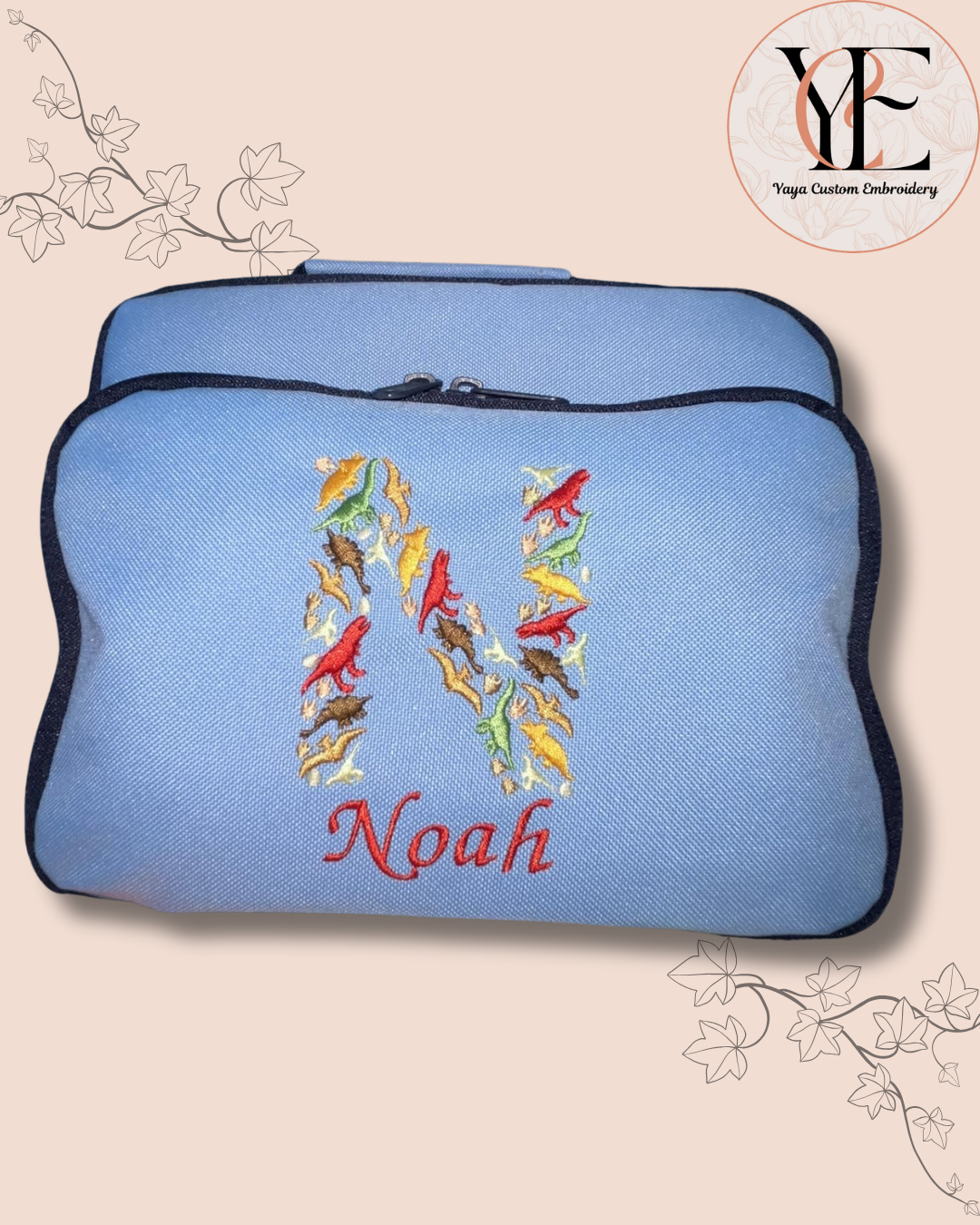 Blue lunch bag with colourful dinosaurs initial  and 'Noah' text on a beige background