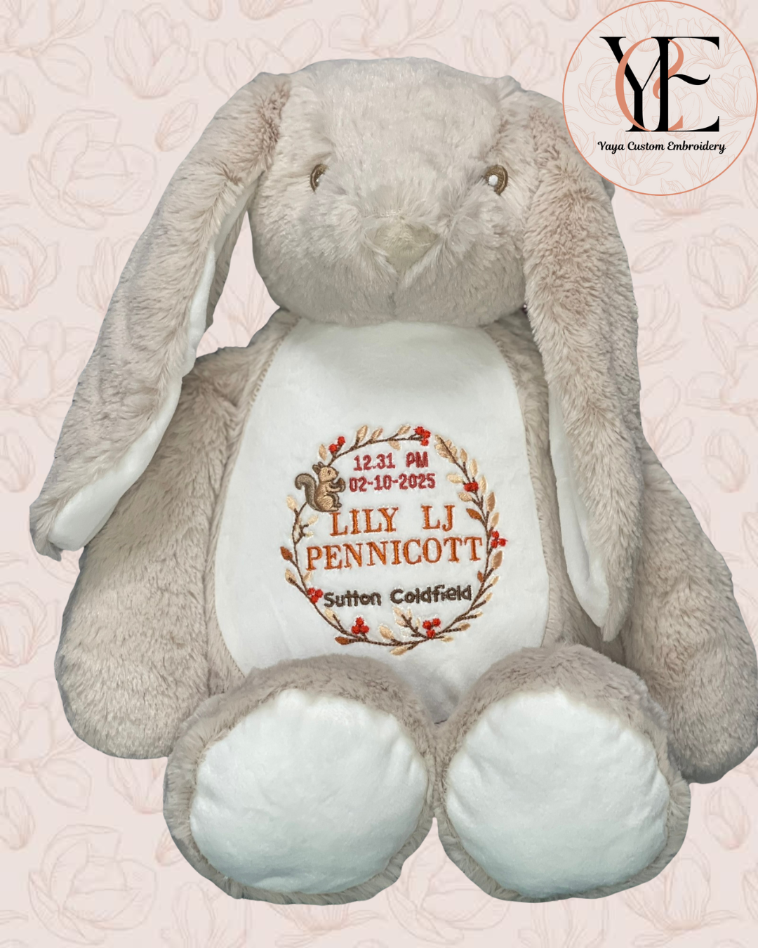 Plush keepsake toy Bunny with the new born details embroidered on its belly using threads with the autumn colours depicting a squirrel holding a pinecone and a wreath with autumn leaves and berries