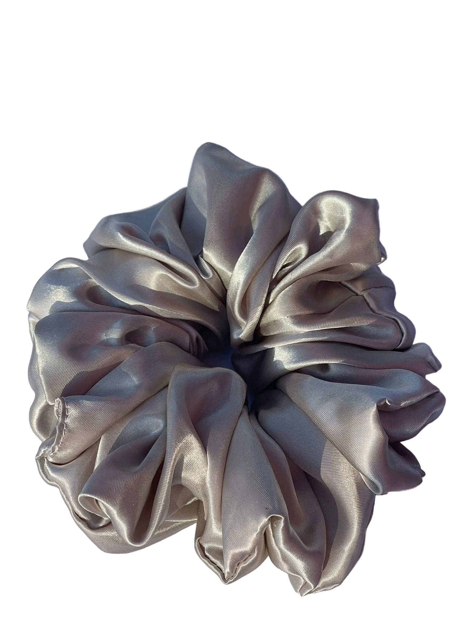 A single satin hair scrunchie in a champagne beige color, laid flat on a white fabric background with a soft shadow cast to the upper right.