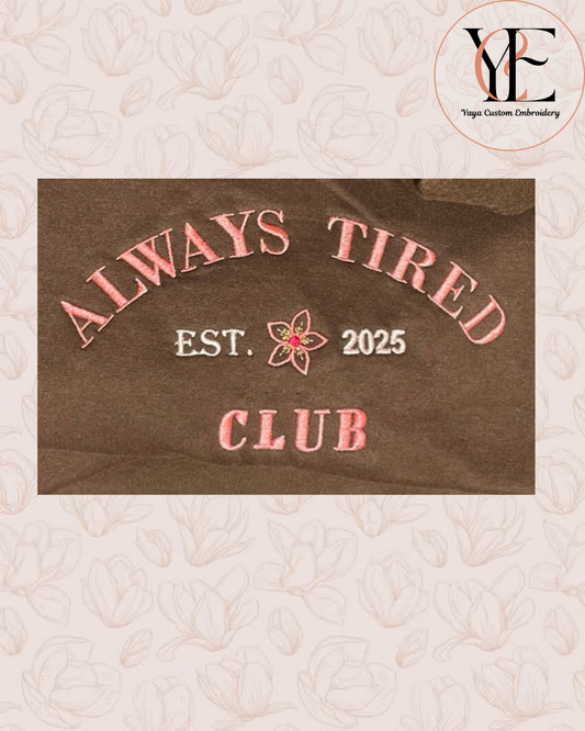Close up of 'Always Tired Club' text  embroidered on a brown sweatshirt. Created by Yaya Custom Embroidery