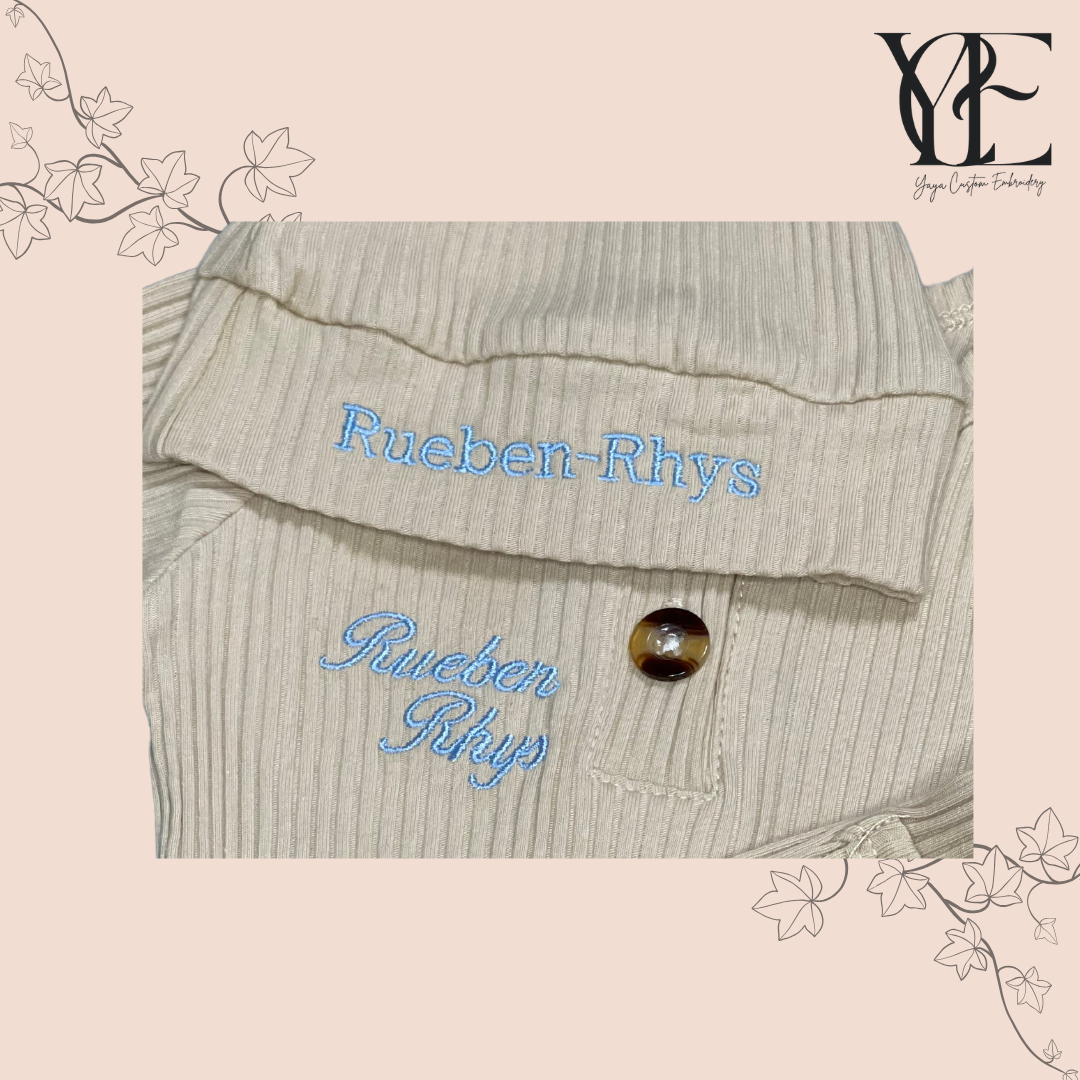 Personalised embroidery in blue of a cream babygrow and hat. By Yaya Custom Embroidery.