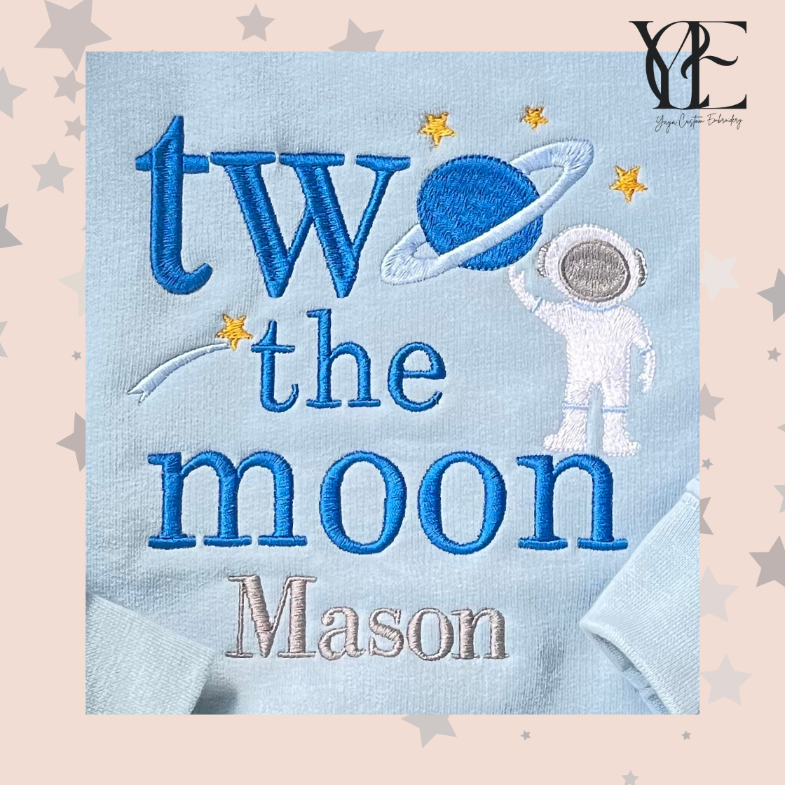 Close-up view of "two the moon" embroidery sweatshirt that depicts the words "two the moon" (where the "o" of "two" is a planet) an astronaut and the child's name, Mason. 