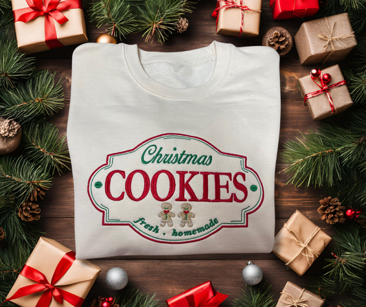 Folded up Christmas cookie label embroidered sweatshirt on a Christmas background with presents, pine cones, Christmas tree branches and Christmas balls. 