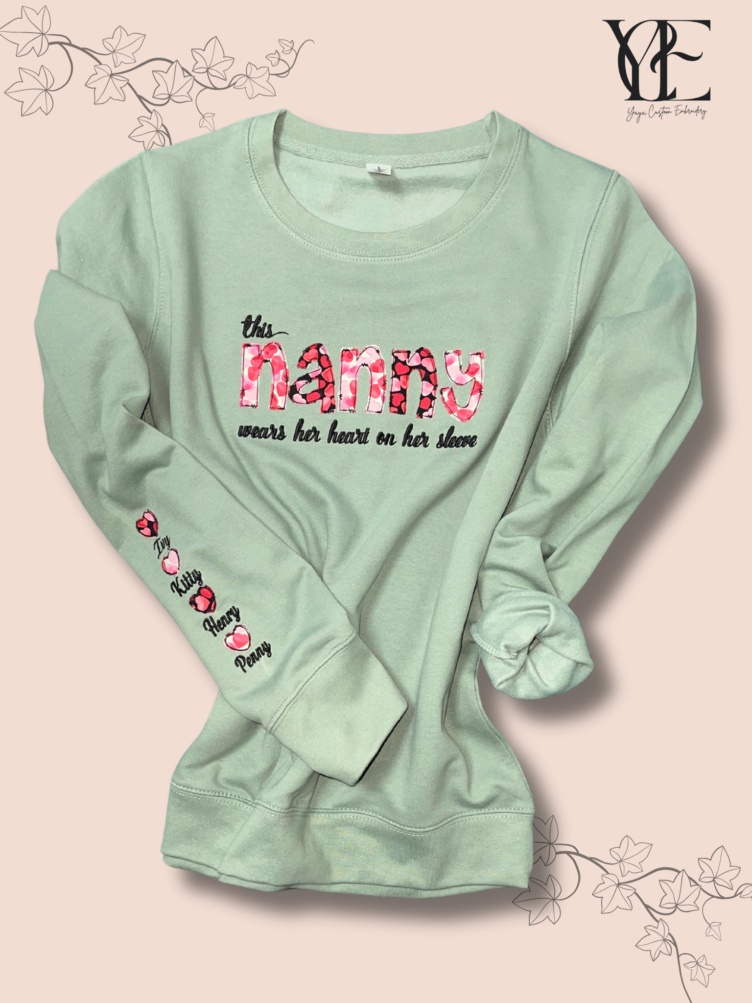 Dusty green sweatshirt personalised on the chest with "This nanny wears her heart on her sleeve" embroidery while the sleeve has the names of her grandchildren.