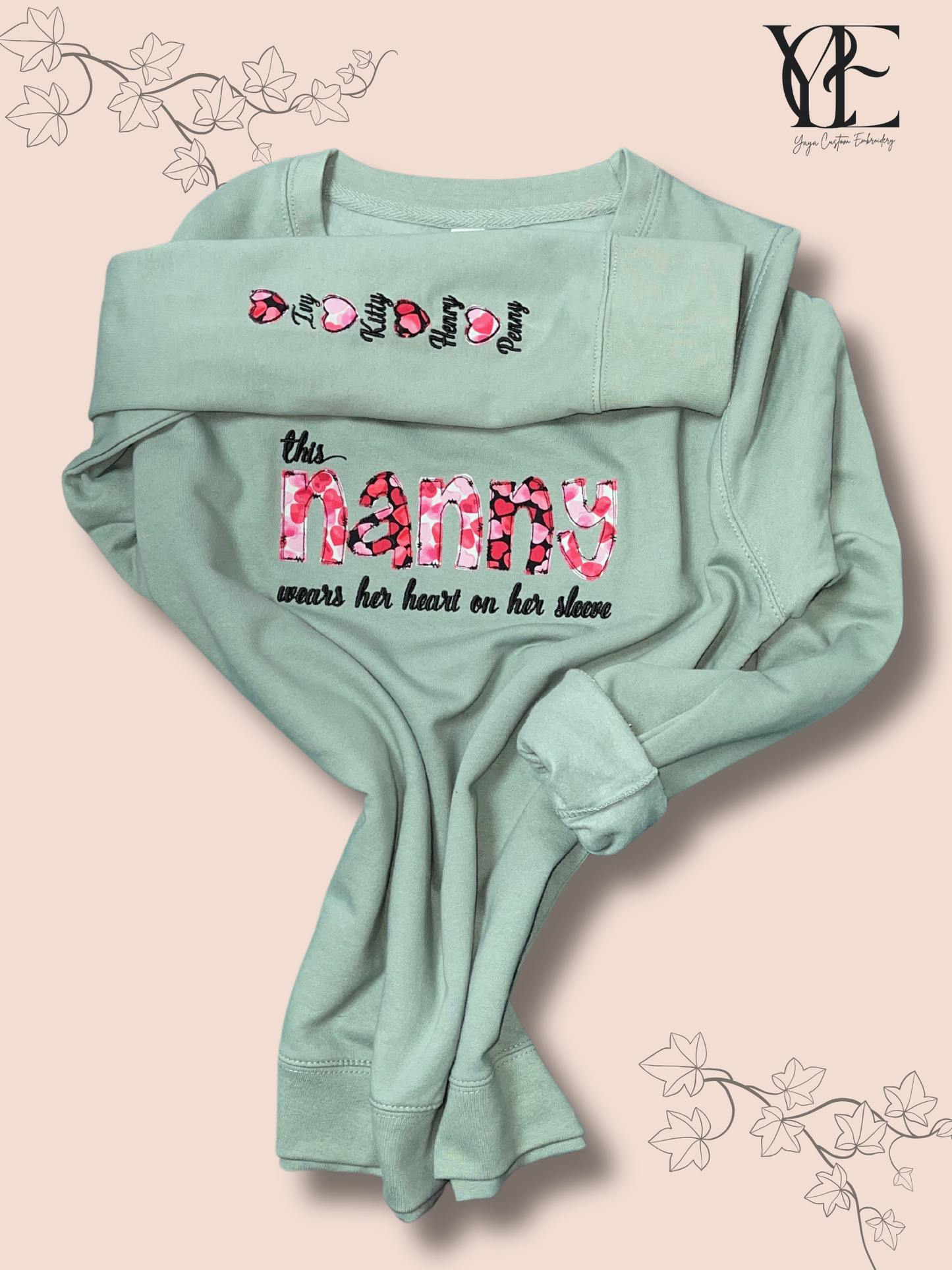 Dusty green sweatshirt embroidered  on the chest with "This nanny wears her heart on her sleeve" while the sleeve has the names of her grandchildren.