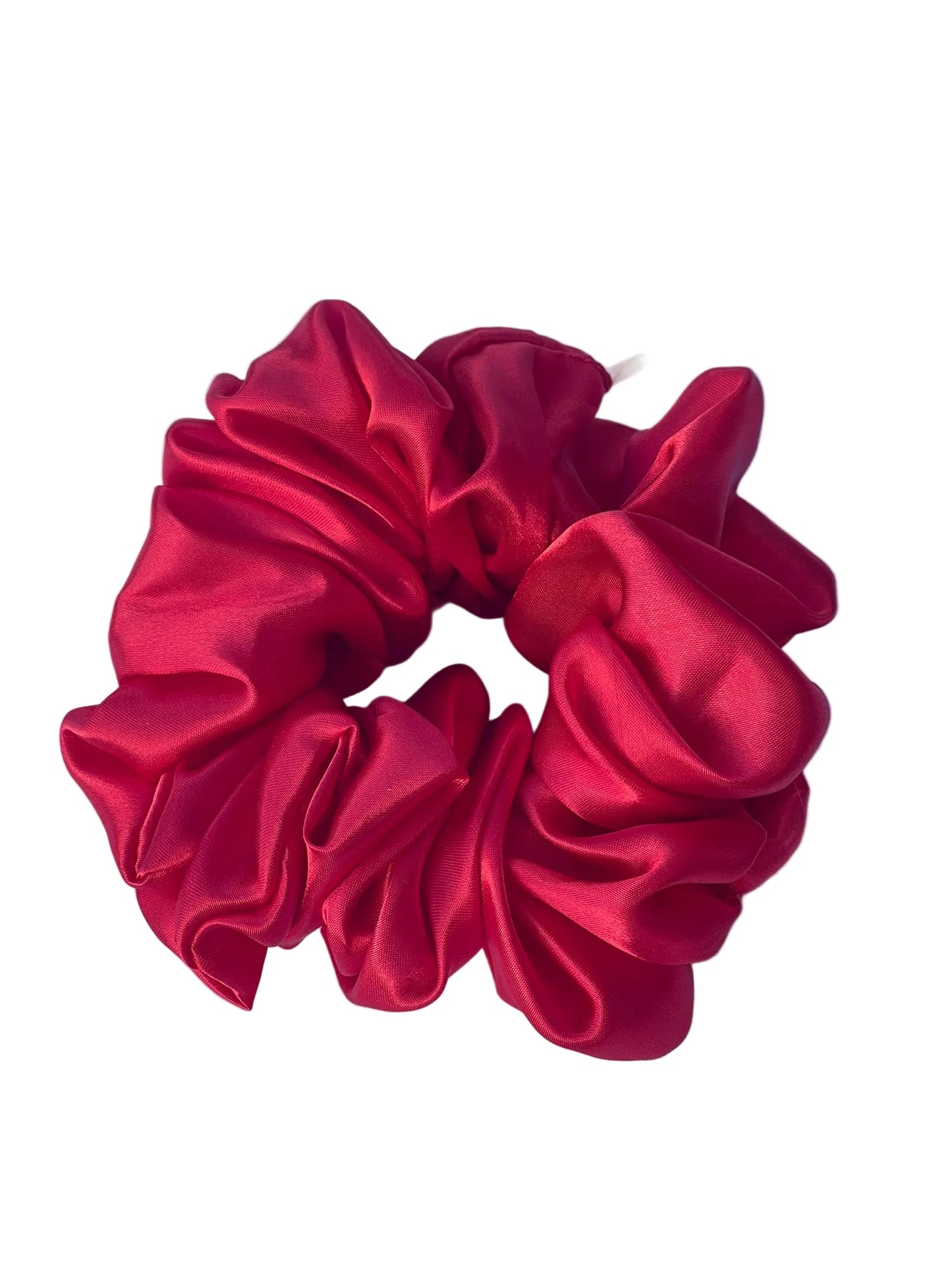 A single red satin hair scrunchie resting on a white fabric background.