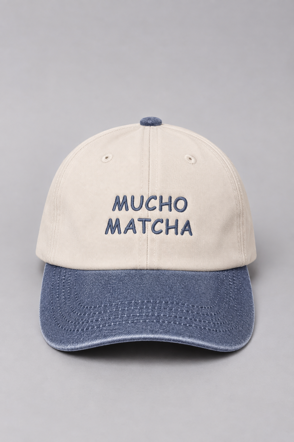 A soft unstructured crown baseball cap with an off-white crown and a denim curved brim. The front of the cap features the words 'MUCHO MATCHA' embroidered in denim.