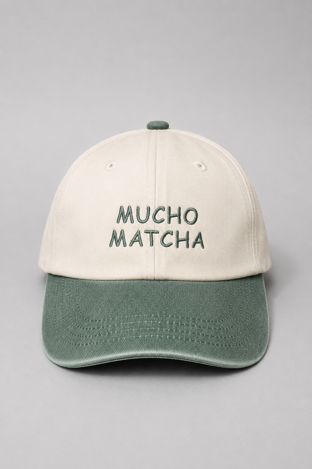 A soft unstructured crown baseball cap with an off-white crown and a bottle green curved brim. The front of the cap features the words 'MUCHO MATCHA' embroidered in green.