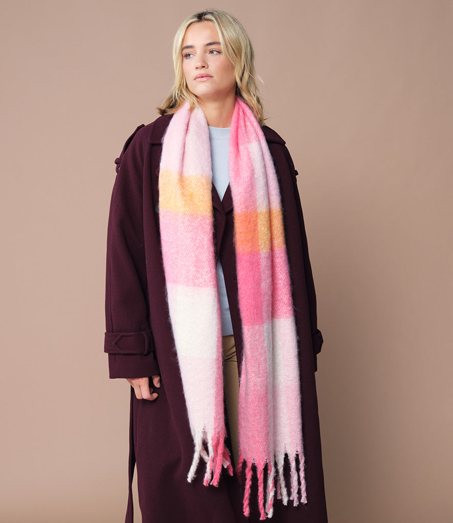 Woman wearing a long, pink check scarf with a plain background