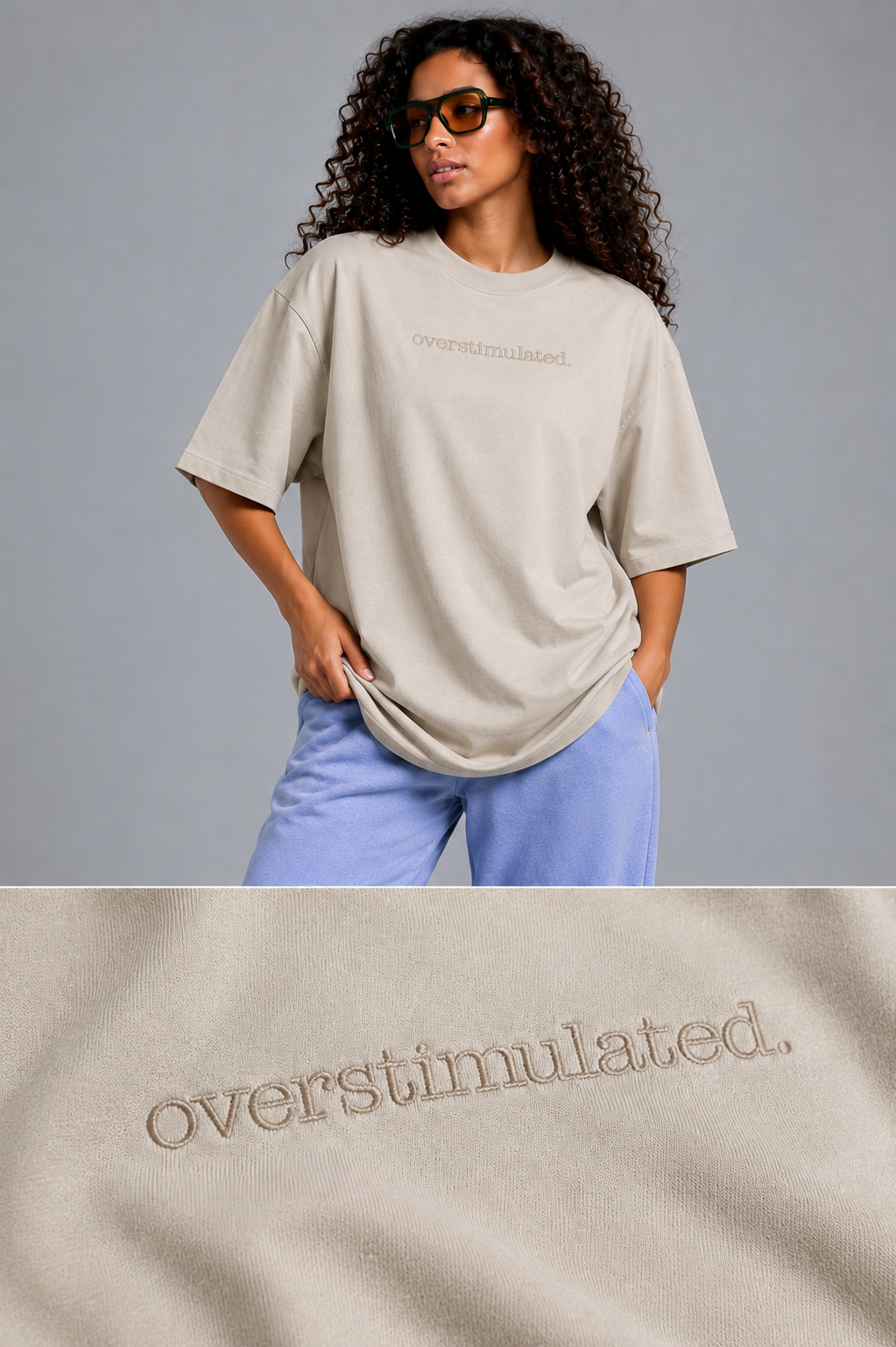 A woman wearing an oversized beige t-shirt with 'overstimulated.' embroidered on the chest, paired with light blue pants, against a solid gray studio background.
