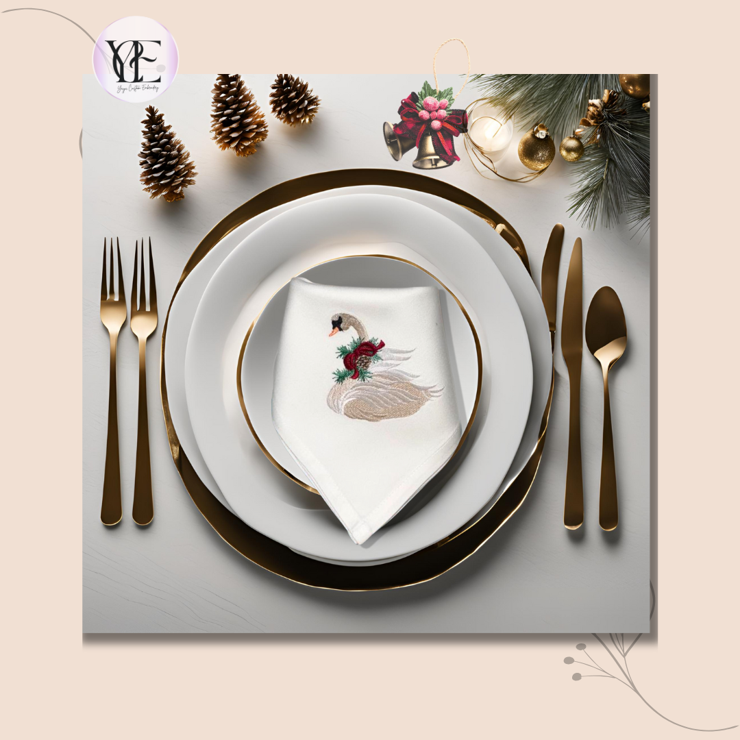 Dinner table set with knifes, forks, spoon, plates and an embroidered swan on a white napkin on top. There are also pine cones and Christmas themed bells.