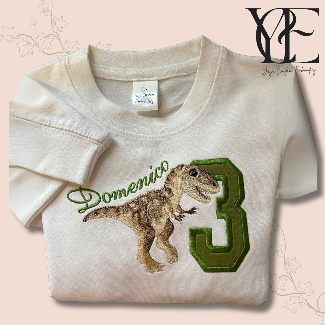 White sweatshirt with a T-Rex dinosaur embroidered and a number 3 and Domenico, the name of the kid is embroidered above the T-Rex back