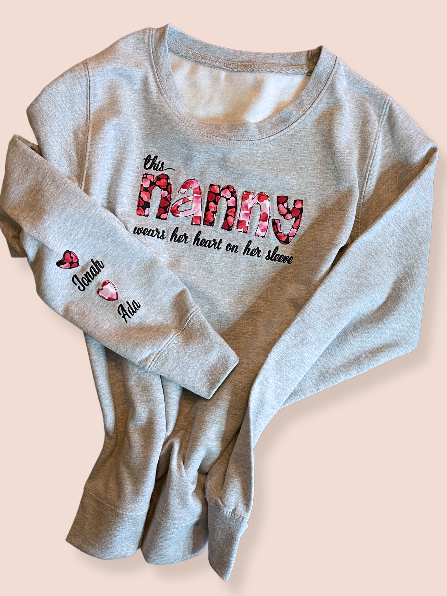 Grey sweatshirt  embroidered with "this nanny wears her heart on her sleeve" on the chest and two names on the sleeve