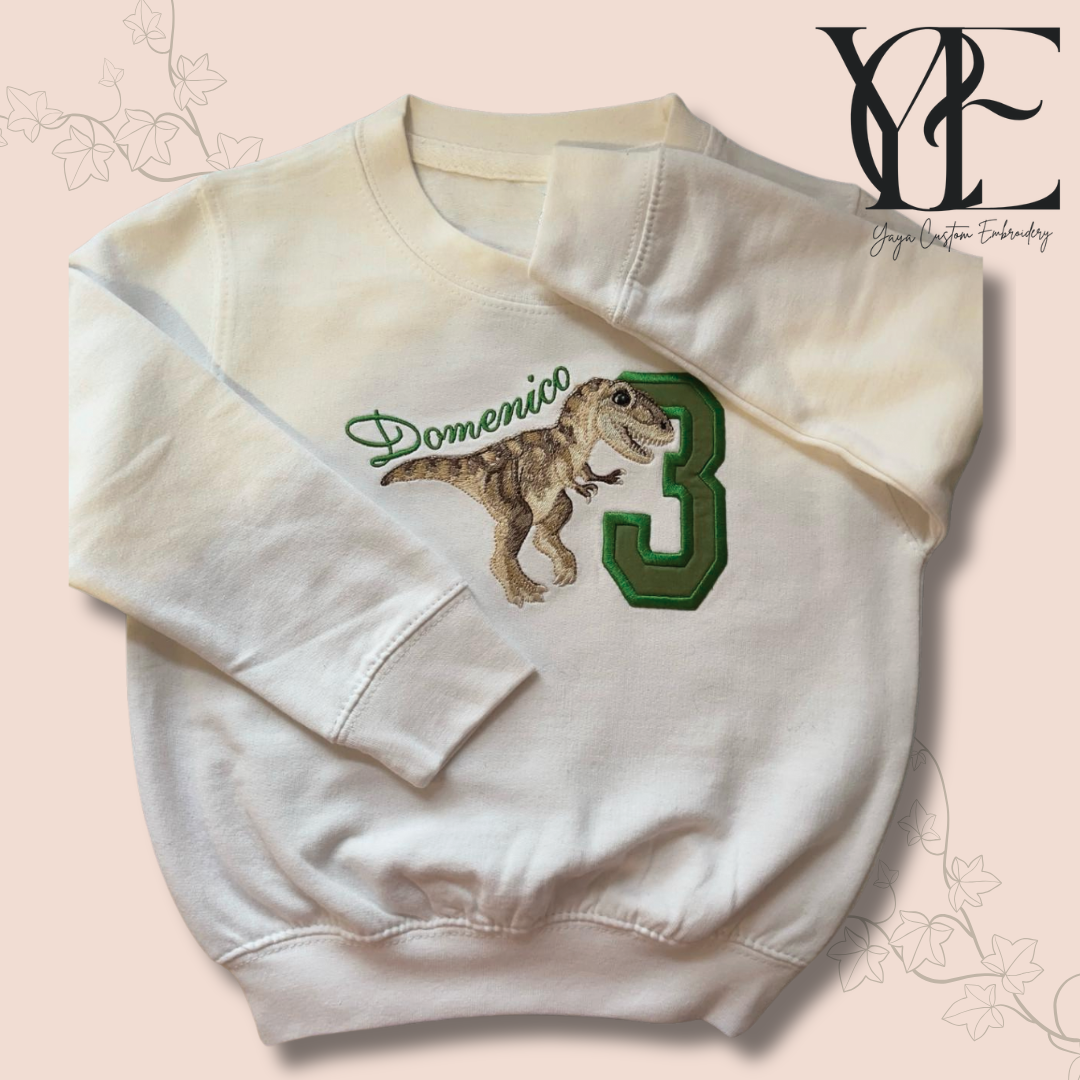 Photo of a white sweatshirt with a T-Rex, the number 3 and the name Domenico embroidered